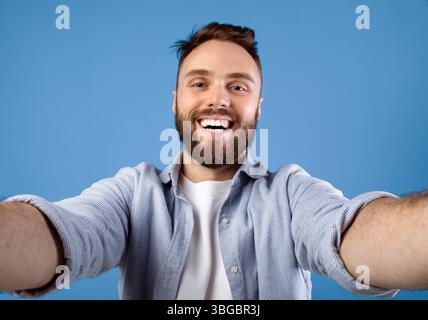 Joyful bearded guy taking selfie on blue studio background Stock Photo