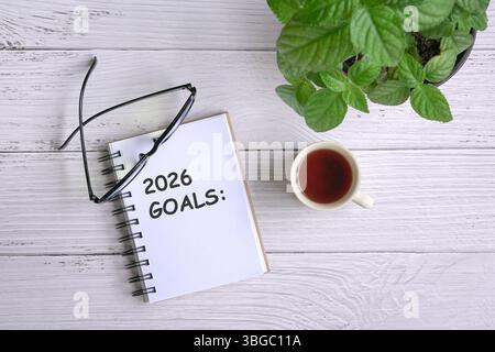 2026 goals on notepad. With eyeglasses, coffee and green plant on white wood table. Top view. Stock Photo