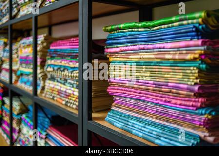 Colorful stacks of traditional Uzbek ikat fabrics on shelves in a textile store, showcasing vibrant patterns and rich cultural heritage of Uzbekistan Stock Photo