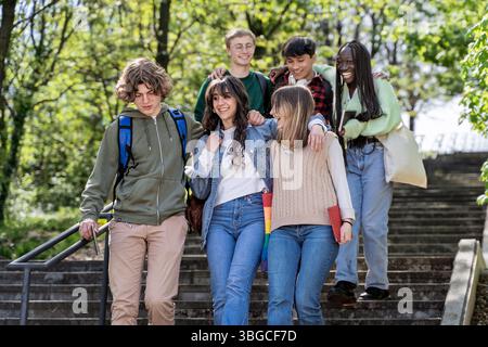 Joyful and diverse group of college students, featuring an LGBTQ rainbow pride bag strap, interacting and walking together on campus. Concepts of yout Stock Photo