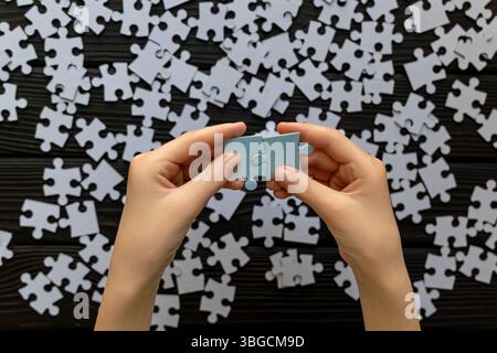 Hands Connecting Puzzle Pieces Over Scattered Jigsaw. Close-up of hands joining two puzzle pieces with scattered pieces in background. Stock Photo