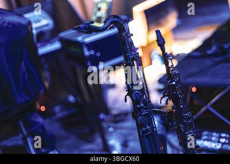 Two saxophones stand ready on stage bathed in blue light, anticipating the arrival of musicians for a performance Stock Photo