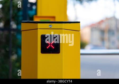 Detailed view of a yellow turnstile gate showing a red "X" LED display, indicating access denied at an outdoor urban entrance. Stock Photo