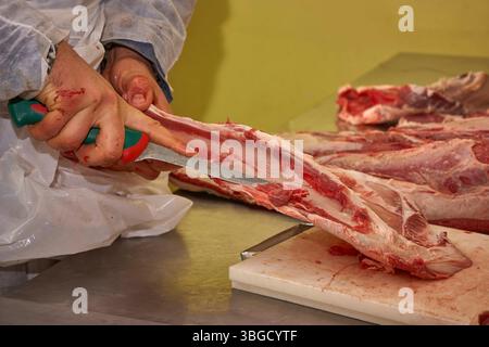 Butcher preparing meat in a butchery, cutting ribs with a knife Stock Photo