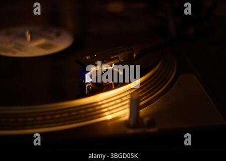 Turntable needle playing a vinyl record in warm lighting, evoking nostalgia and music enjoyment Stock Photo