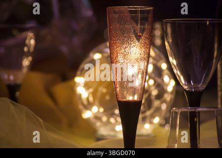 Romantic atmosphere created by a champagne flute and a wine glass illuminated by warm string lights Stock Photo