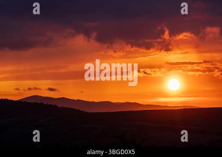 Vast mountain landscape at sunset with glowing sun over layered hills and colorful sky, ideal for travel and panoramic scenes Stock Photo