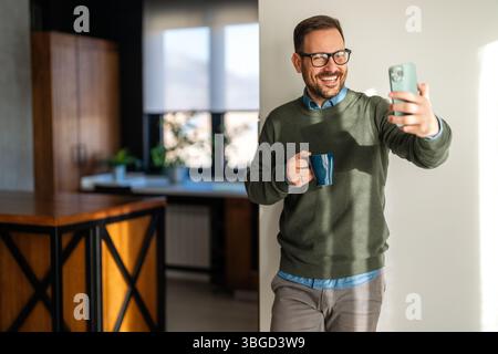 Confident smiling businessman using smartphone in a home office. Checking new e-mails, video call Stock Photo