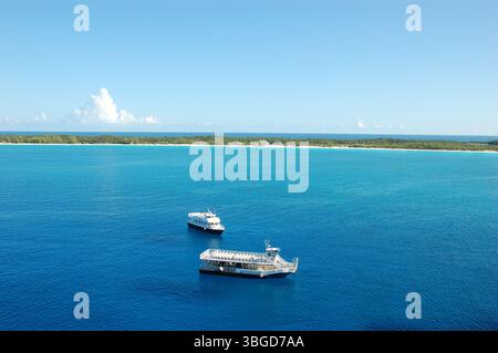 Two small boats floating on calm turquoise waters near a tropical island with white sandy shore and lush greenery Stock Photo