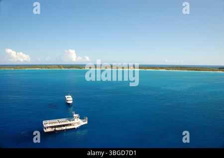 Two small boats floating on calm turquoise waters near a tropical island with white sandy shore and lush greenery Stock Photo