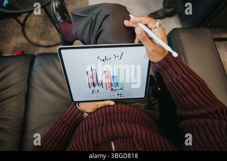 Close-up of a person using a tablet to analyze sales data with colorful bar graphs in a professional office setting Stock Photo