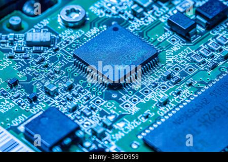 Milan, Italy 1 January 2025: Electronic circuit board with microchip, resistors, and capacitors, bathed in blue light, showcasing intricate details of Stock Photo