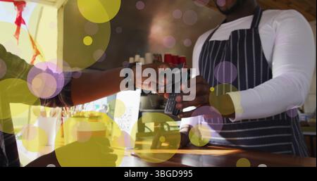 Image of falling yellow dots over people using payment terminal Stock Photo