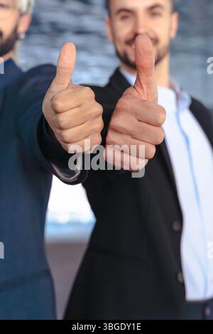 Two confident businessmen in suits giving thumbs up and smiling at camera Stock Photo