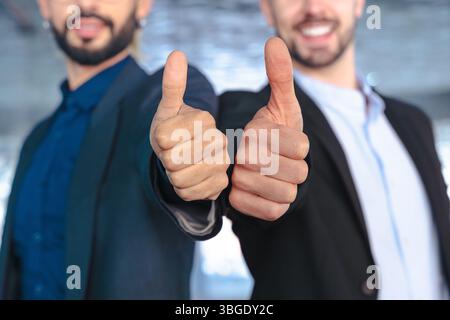 Two confident businessmen in suits giving thumbs up and smiling at camera Stock Photo