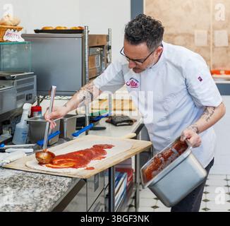 Italian Chef Preparing Artisan Pizza Dough with Tomato Sauce in a Bakery Kitchen Stock Photo
