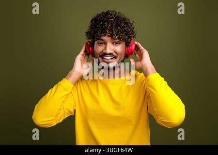 Young man in yellow shirt wears headphones and smiles joyfully against a green background for lifestyle concepts Stock Photo