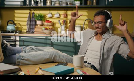 African American ethnic man happy carefree young male student gen z teen in headphones dancing moving at home kitchen studying relaxed guy music in Stock Photo