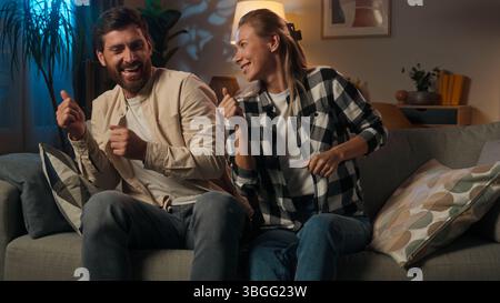 Happy family Caucasian woman man dancing at home evening carefree relationship couple dance on couch singing fun music father mother wife husband Stock Photo