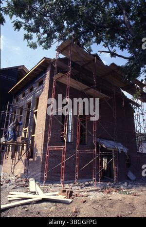 A worker stands on scaffolding preparing to lay bricks on the exterior of an older brick home being renovated. This image shows the detailed brickwork restoration process in progress. Stock Photo