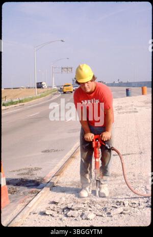 A construction worker uses a jackhammer on a section of I-670 during construction in 1980. The worker is wearing a hard hat and safety gear. Stock Photo