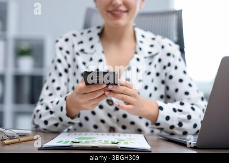 Woman taking photo of document using scanning app on smartphone at desk in office, closeup Stock Photo