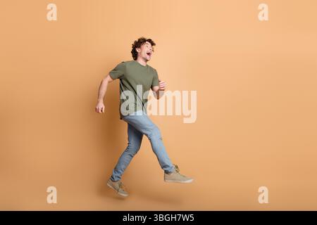 Energetic young man in casual outfit smiling and walking joyfully against a beige background Stock Photo