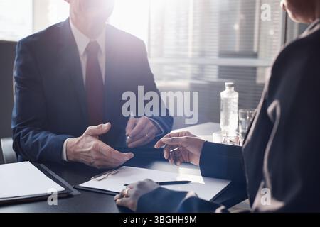 Over shoulder shot of Black woman and Caucasian man wearing suits discussing business documents at office table Stock Photo