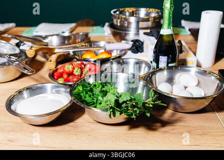 Various fresh ingredients including strawberries, eggs, sugar, and mint laid out in bowls, ready for making a dessert recipe. Stock Photo