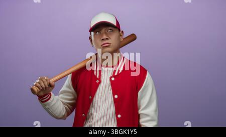 Young man in baseball uniform with bat expresses emotion against a purple background, highlighting sport and fashion in an isolated setting. Stock Photo
