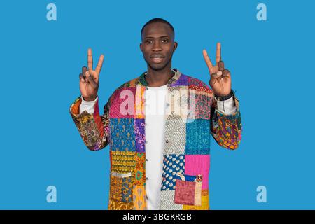 Portrait of stylish young man gesturing peace sign with both hands on blue background Stock Photo