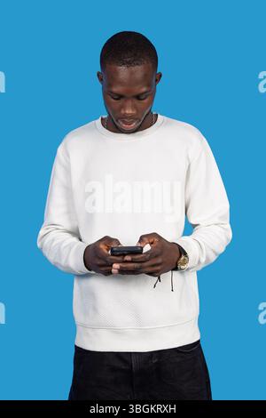 Young man using smartphone on blue background: concentrated casual black man browsing internet on mobile phone Stock Photo