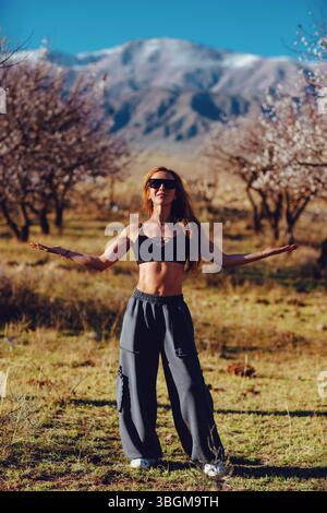 Young beautiful fitness woman posing in blooming garden on mountains background Stock Photo