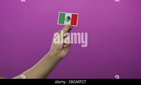 Man hand holding mexican flag embroidery against a vibrant pink wall, showcasing national pride and craft on an isolated colored background with empha Stock Photo