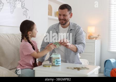 Father giving his daughter pocket money at table indoors Stock Photo