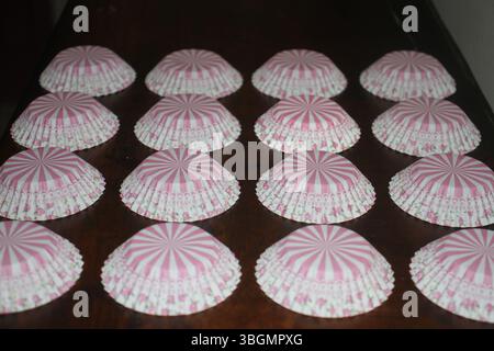 A symmetrical arrangement of pink and white striped cupcake liners placed upside down on a dark wooden surface. Each liner has a striped pattern. Stock Photo