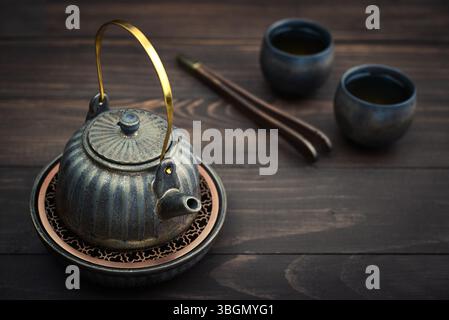 Traditional asian tea ceremony arrangement: ceramic teapot, cups and bamboo chaban on dark wooden background Stock Photo