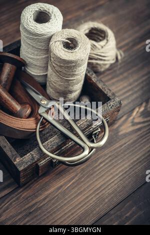 Tools and accessories for handicrafts or gift wrapping: bonsai scissors, jute rope, leather ribbon and spools  in vintage wooden box on dark wooden ba Stock Photo