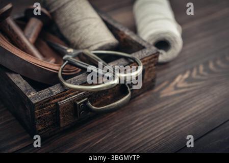 Tools and accessories for handicrafts or gift wrapping: bonsai scissors, jute rope, leather ribbon and spools  in vintage wooden box on dark wooden ba Stock Photo