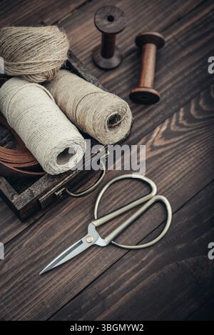 Tools and accessories for handicrafts or gift wrapping: bonsai scissors, jute rope, leather ribbon and spools  in vintage wooden box on dark wooden ba Stock Photo