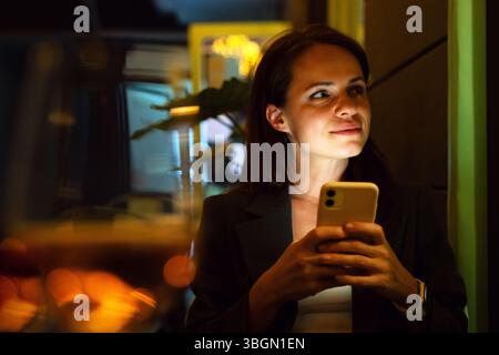 Urban woman using smartphone while sitting in cafe in the evening after work Stock Photo