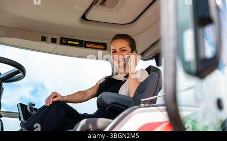 Female agricultural machinery driver talking on mobile phone in cabin Stock Photo