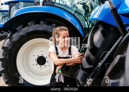 Female technician next to agricultural machinery and using her mobile phone. Stock Photo