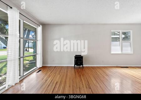 Large, empty living room with a black stove in the middle. The room is very clean and has a lot of natural light coming in through the windows Stock Photo