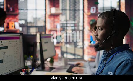 Diverse customer center workers assisting clients with installing software. Multiethnic team of call center agents using remote access tools to connect to customer devices, fixing errors, camera B Stock Photo