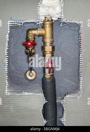 Newly installed brass water pipes plumbing with red tap fittings, gray cement wall reinforced with plastic mesh around, closeup detail Stock Photo