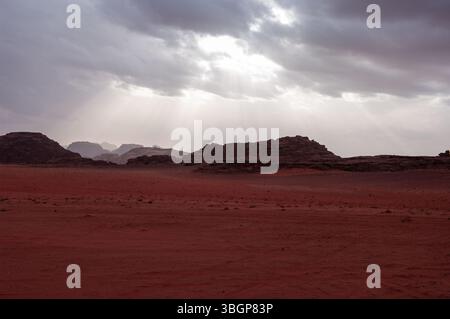 A desert landscape with a cloudy sky and mountains in the background. The sky is overcast and the sun is shining through the clouds Stock Photo