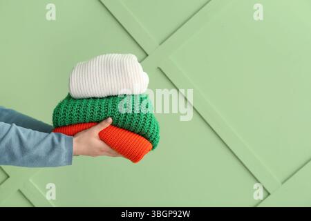 Female hands with stack of different stylish sweaters on green background Stock Photo
