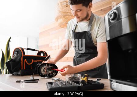 Male worker repairing coffee machine with screwdriver in kitchen Stock Photo