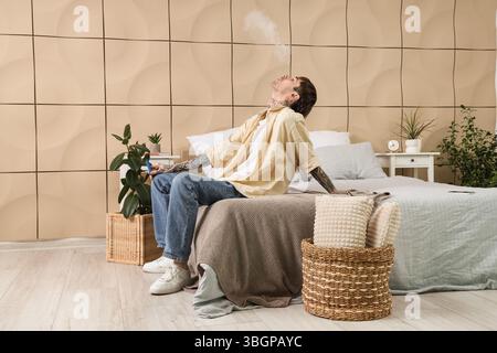 Young man smoking disposable electronic cigarette and resting on bed at home Stock Photo
